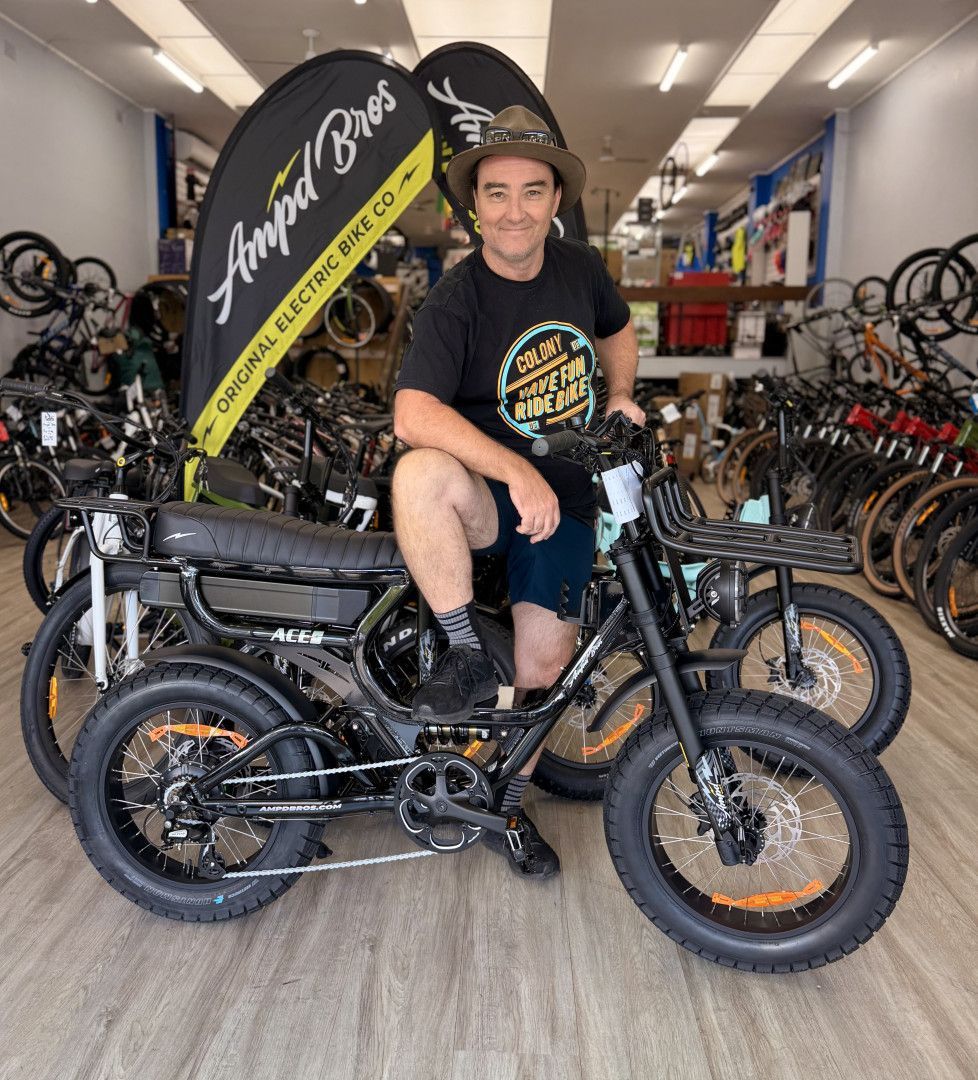 Man sits on black electric bike inside a bike shop — Grafton City Cycles in Grafton, NSW