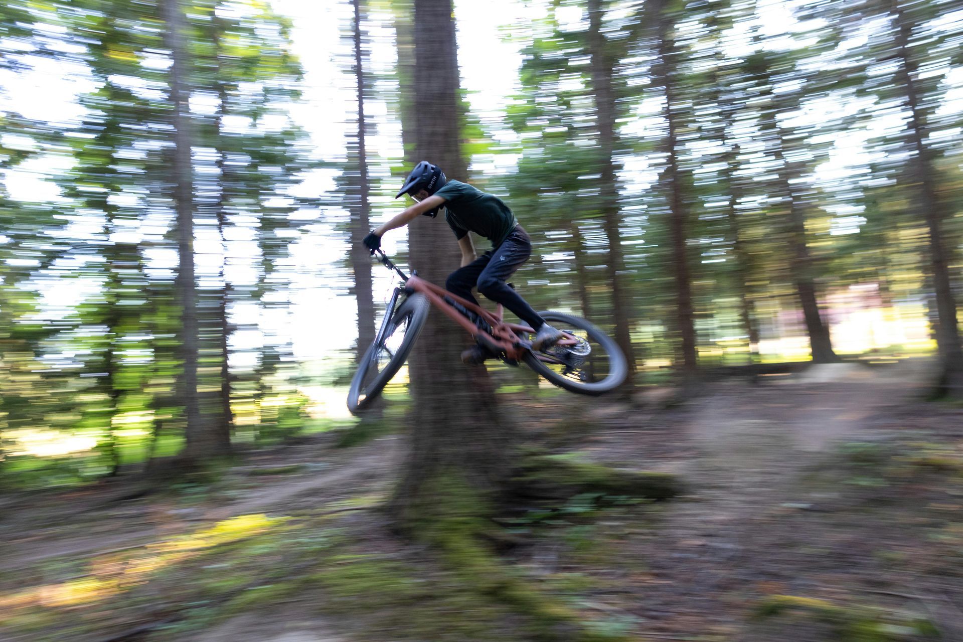 Mountain biker airborne, clearing jump in a forest with blurred background — Grafton City Cycles in Grafton, NSW