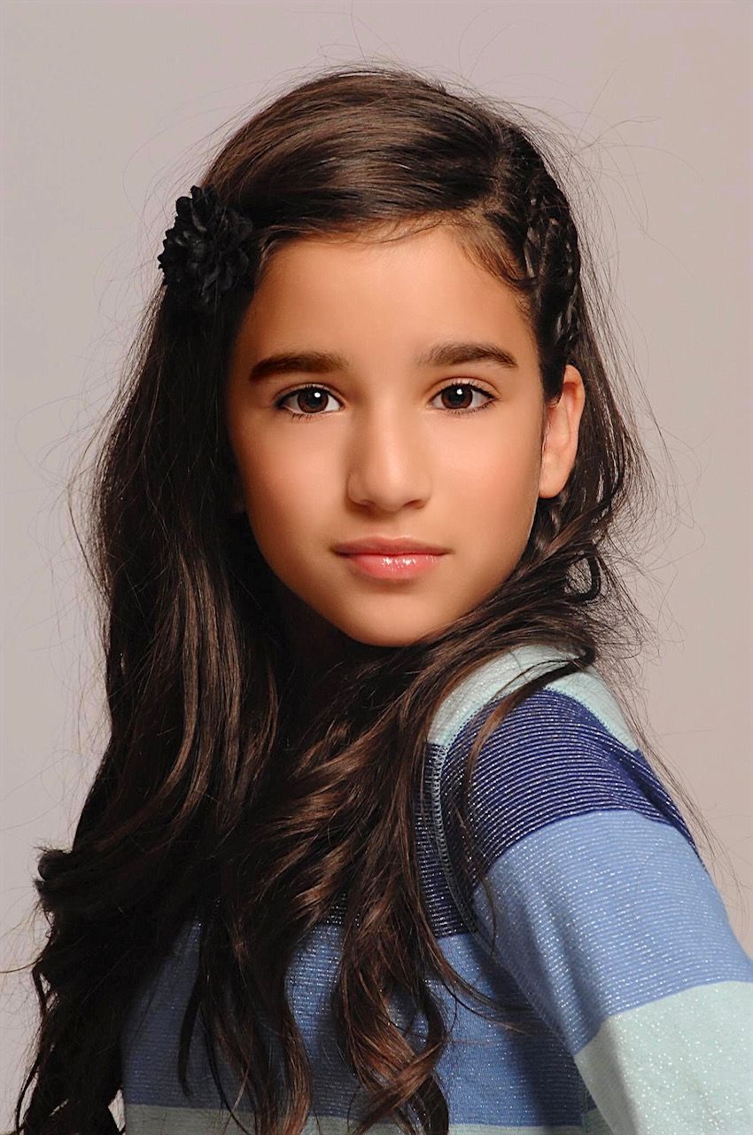 Woman with dramatic eye makeup and gold arm cuffs, lying on a patterned surface.