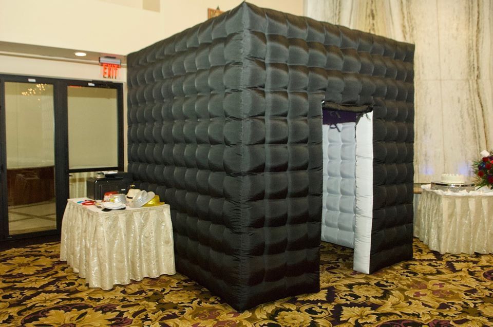 Black inflatable photo booth in a room with a table, next to a door and a window.