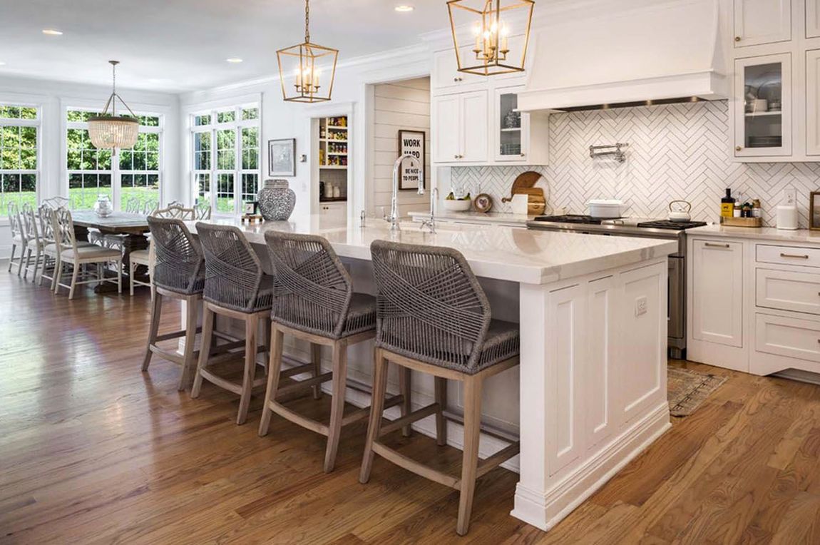 A kitchen with white cabinets , stainless steel appliances , hardwood floors and a large island.