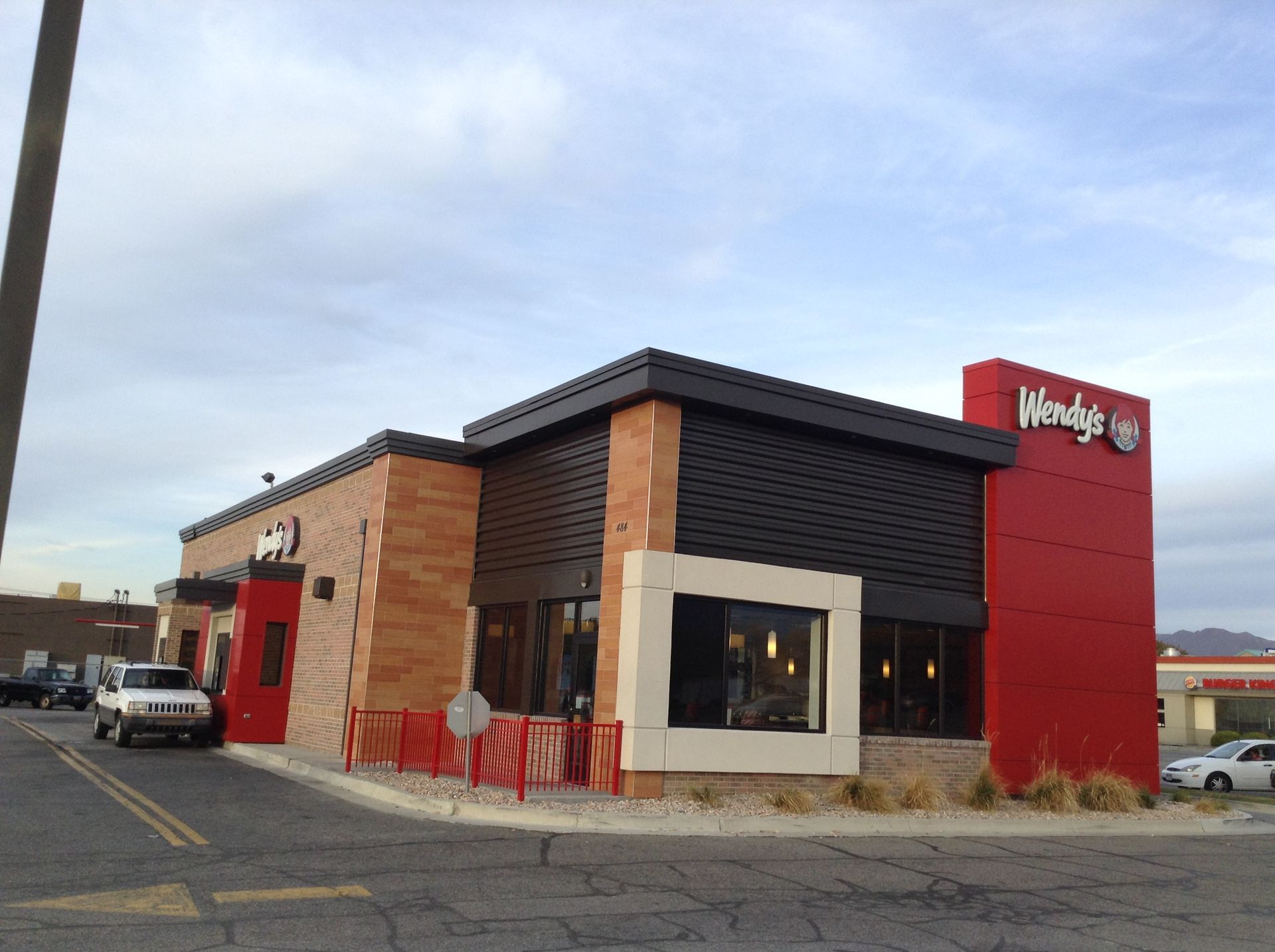 Wendy's restaurant exterior: brick, black, and red facade. Cars in drive-thru, overcast sky.