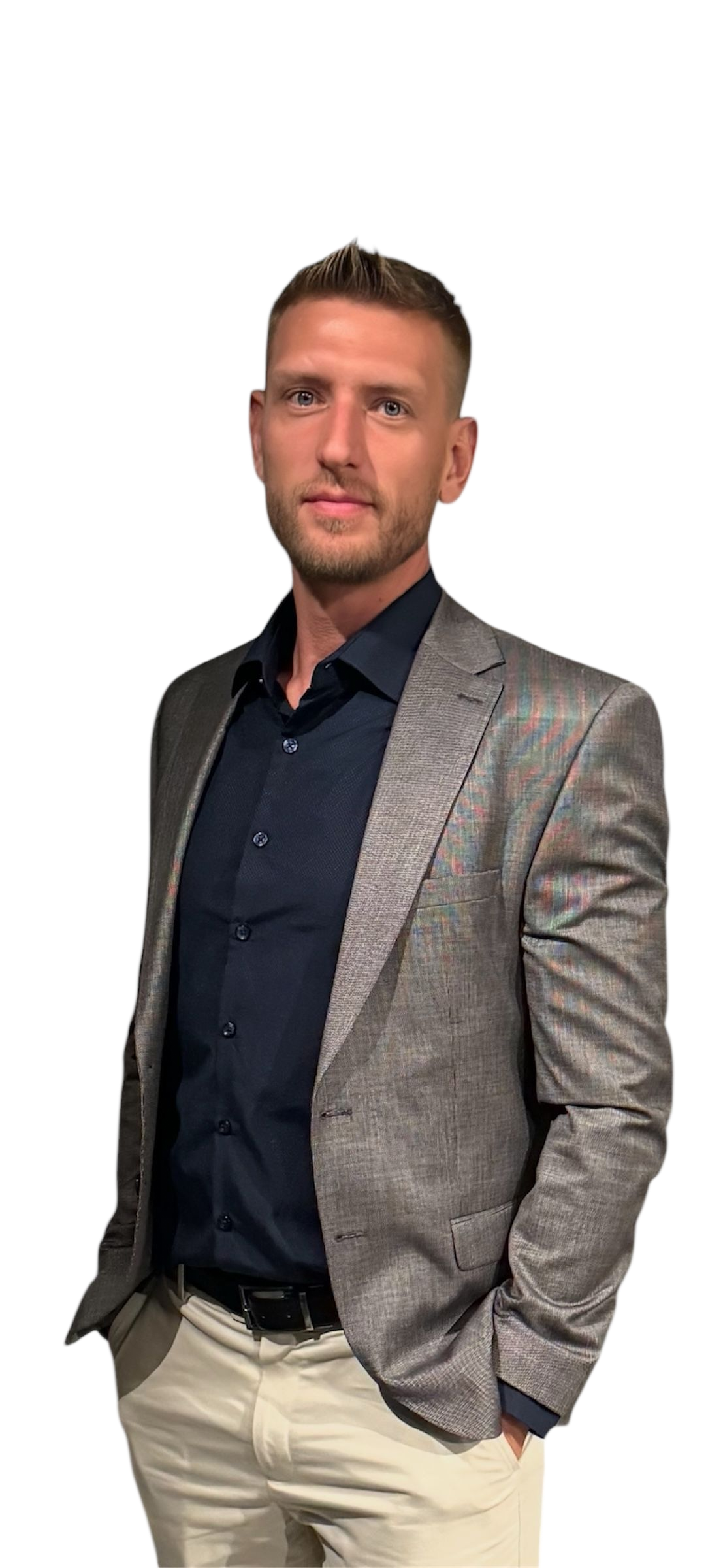 Garett Howell wearing a grey blazer, blue shirt, and khaki pants poses with hands in pockets.