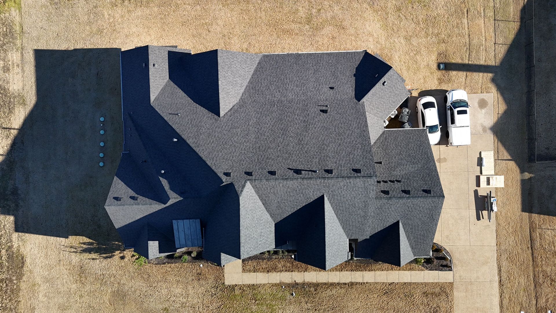 Overhead view of a house with a dark gray roof, two parked cars, and a brown yard.