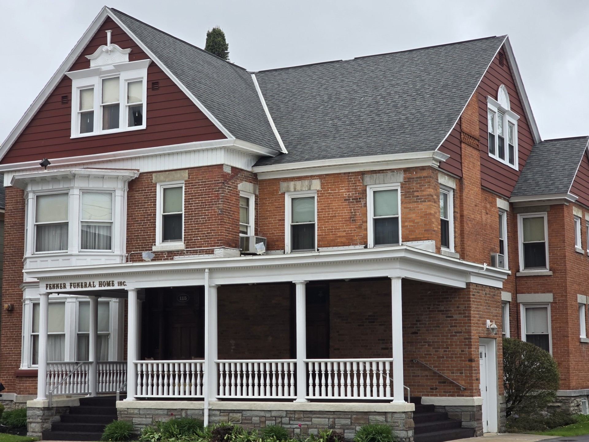 Red brick building with a white porch and dark gray roof. 