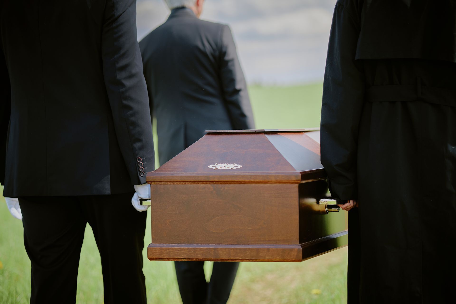 People in black suits carrying a wooden casket outdoors on green grass.