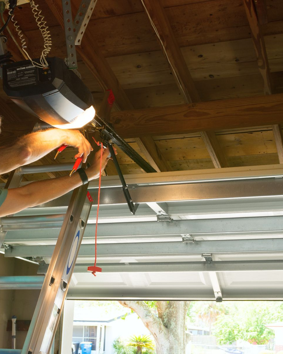 Person on ladder working on garage door opener, indoors.