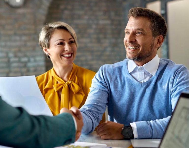 A man and a woman are shaking hands while sitting at a table.