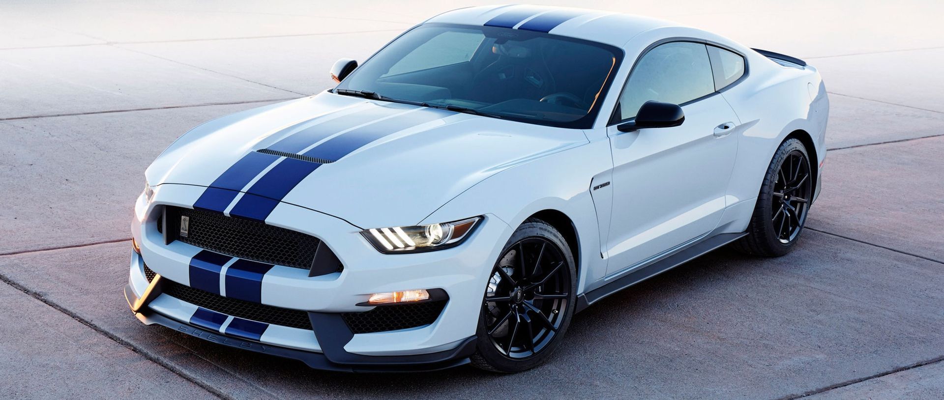 A white ford mustang with blue stripes is parked on the side of the road.