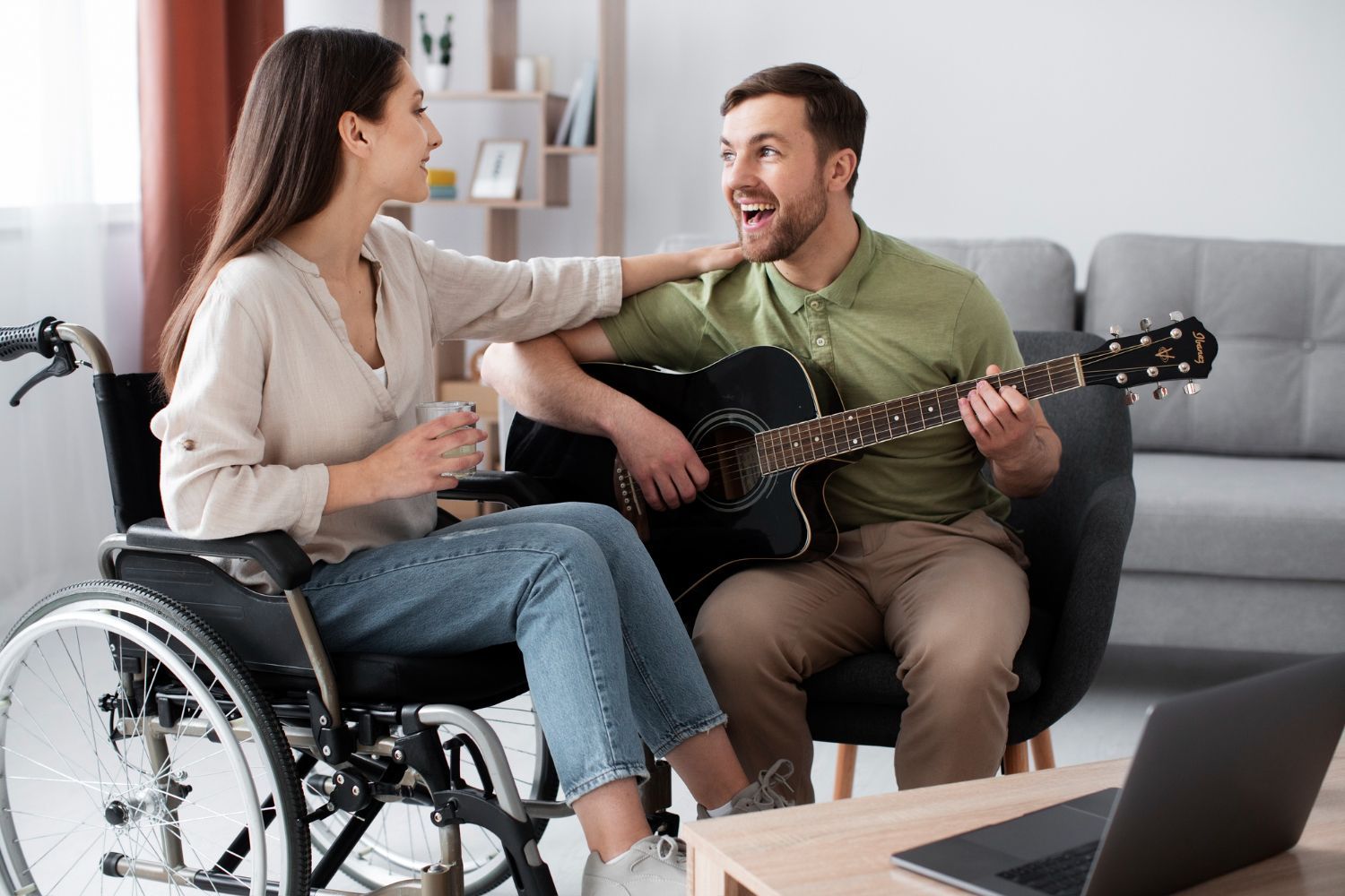 A woman in a wheelchair is sitting next to a man playing a guitar.