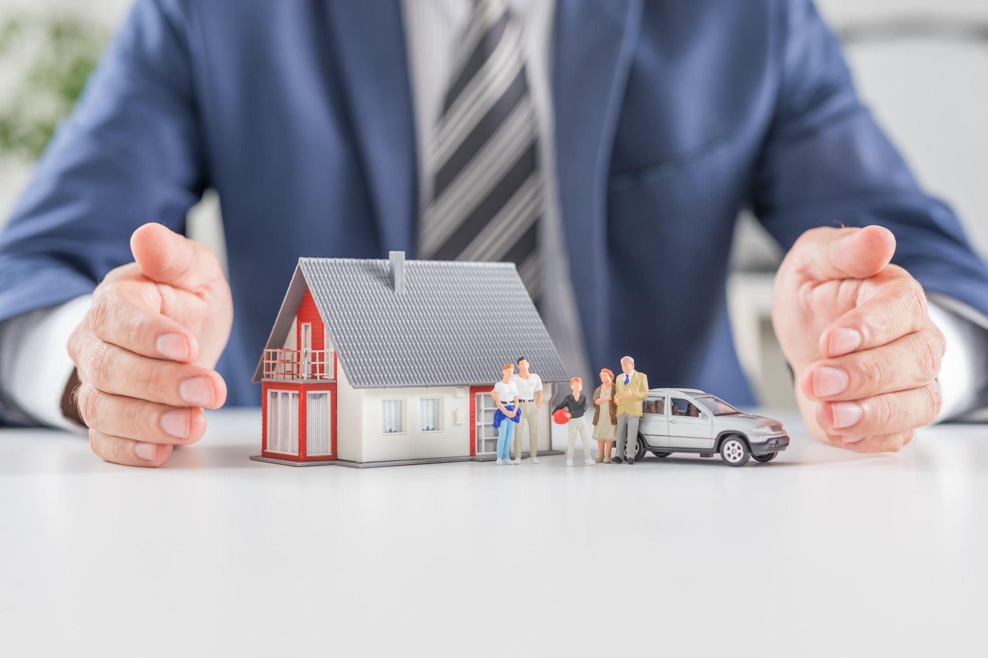 A man in a suit and tie is holding a house and a car.