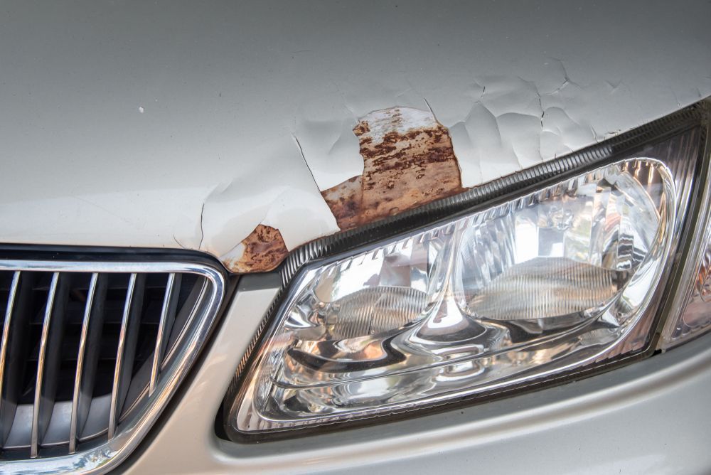 Damaged White Car Front End With Rust Above the Headlight and Grille — FNQ Paintless Dent Repair in Edmonton, QLD