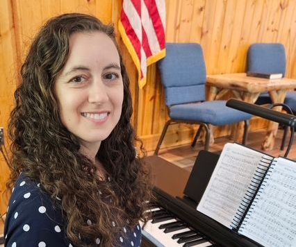 A man in a burgundy suit and a woman in a red sweater smile, posing in front of a wood wall.
