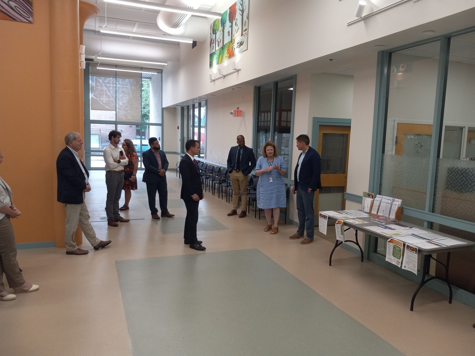 People in a hallway, some in suits, others in casual wear.  They appear to be listening to someone.