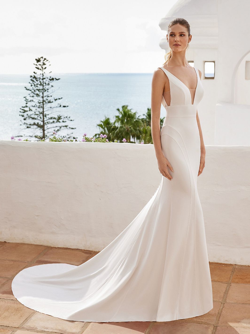 A woman in a white wedding dress is standing on a balcony overlooking the ocean.