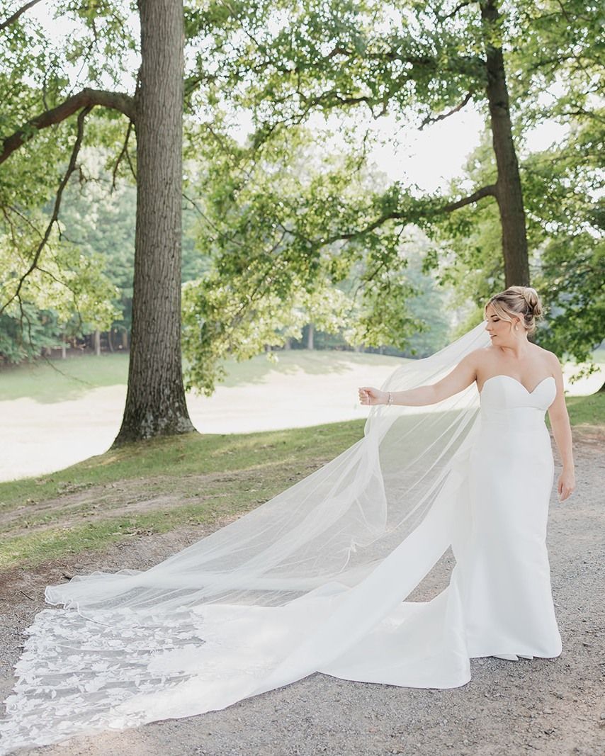 A bride in a wedding dress and veil is standing in a park.