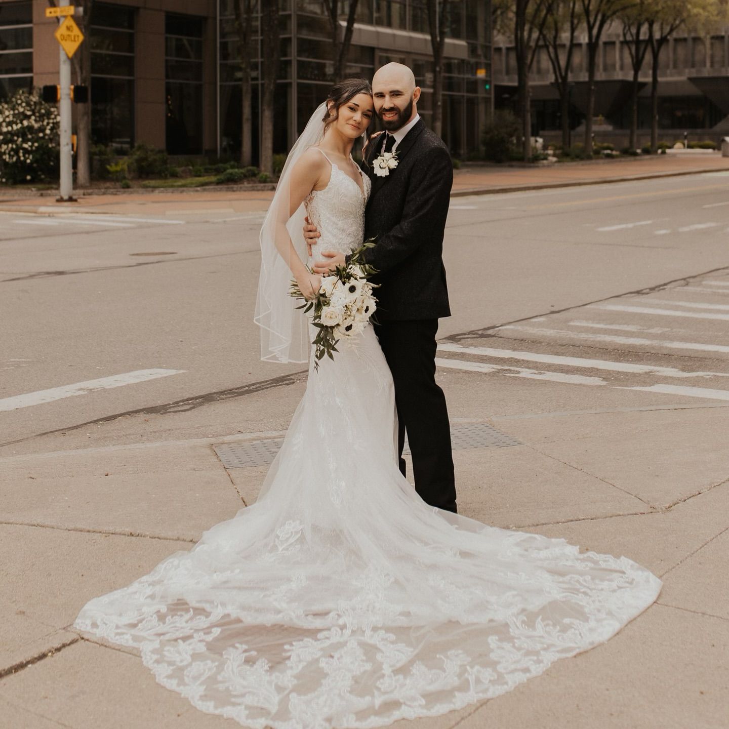 A bride and groom are posing for a picture on the sidewalk.