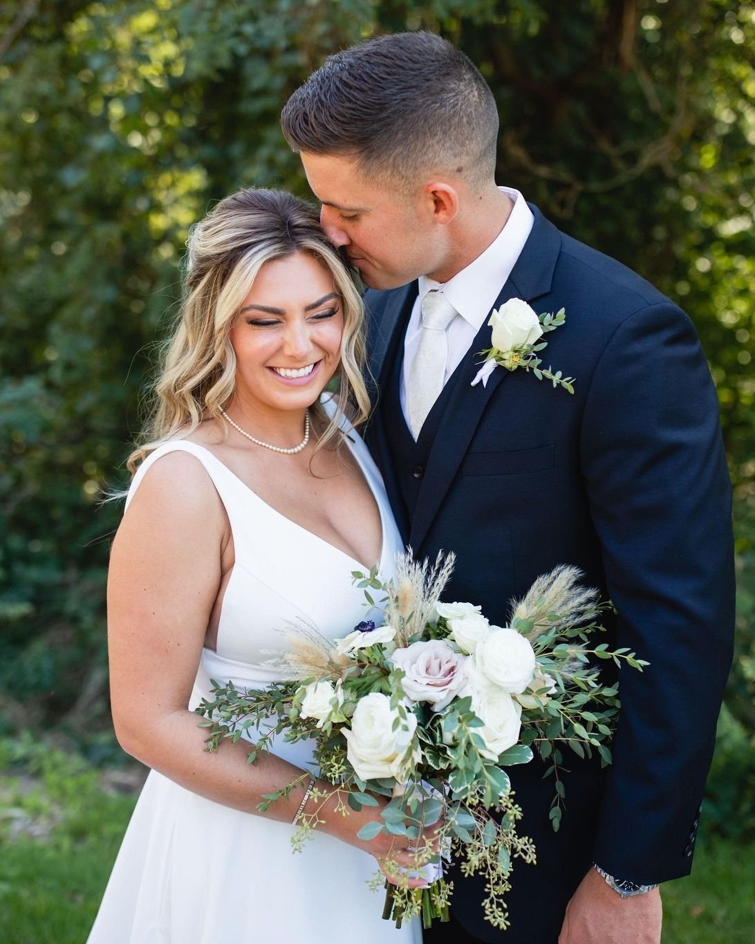 A bride and groom are posing for a picture on their wedding day, the women is smiling.