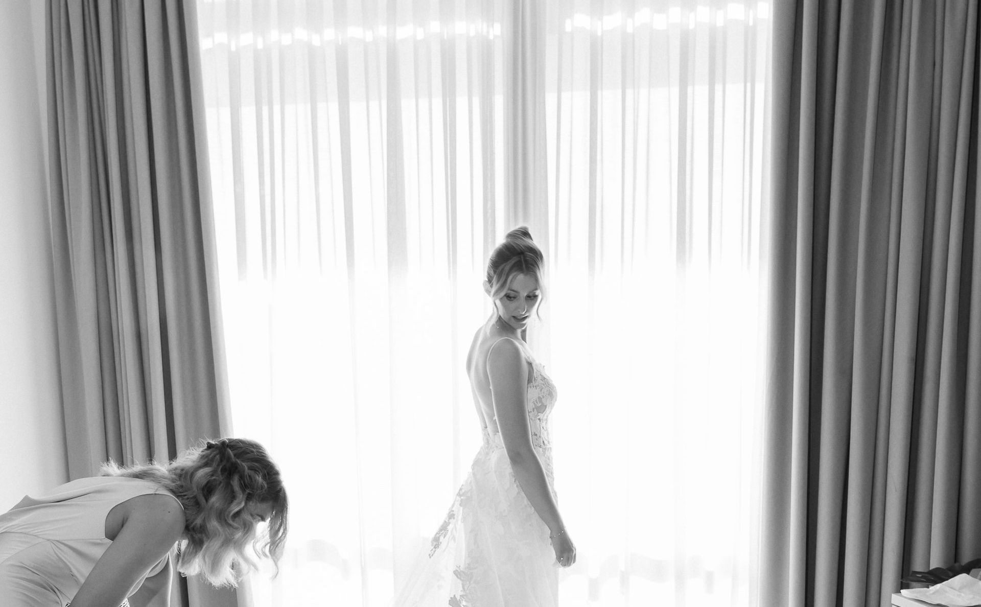 A bride is watching her bridesmaid fix her train
