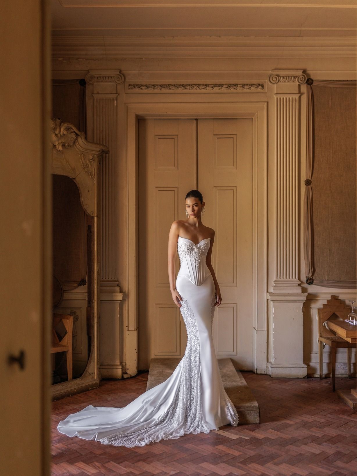 Bride in a white mermaid gown with a long train, standing near a doorway.