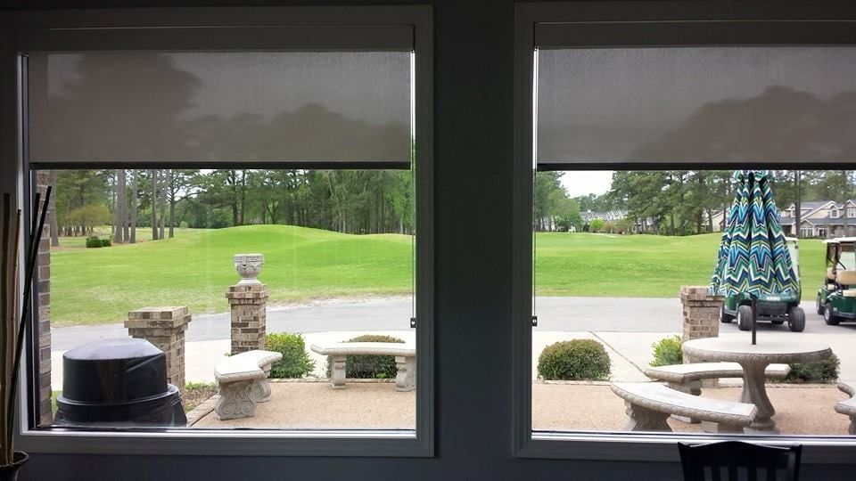 A view of a golf course through two windows with roller shades.