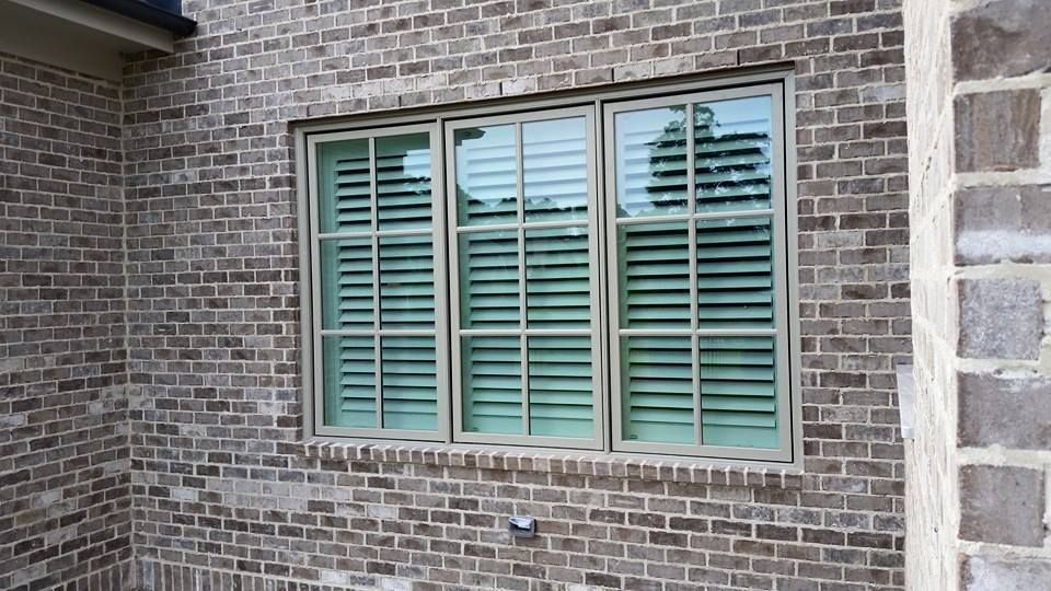 A large window on the side of a brick building with green shutters.
