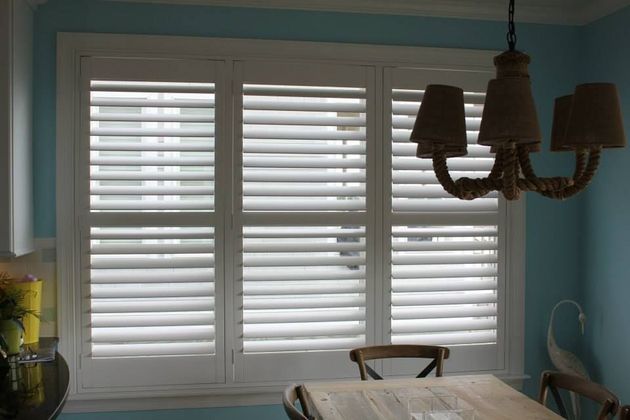 A dining room with white shutters and a chandelier