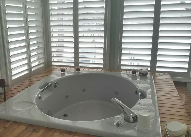 A jacuzzi tub in a bathroom with shutters on the windows.