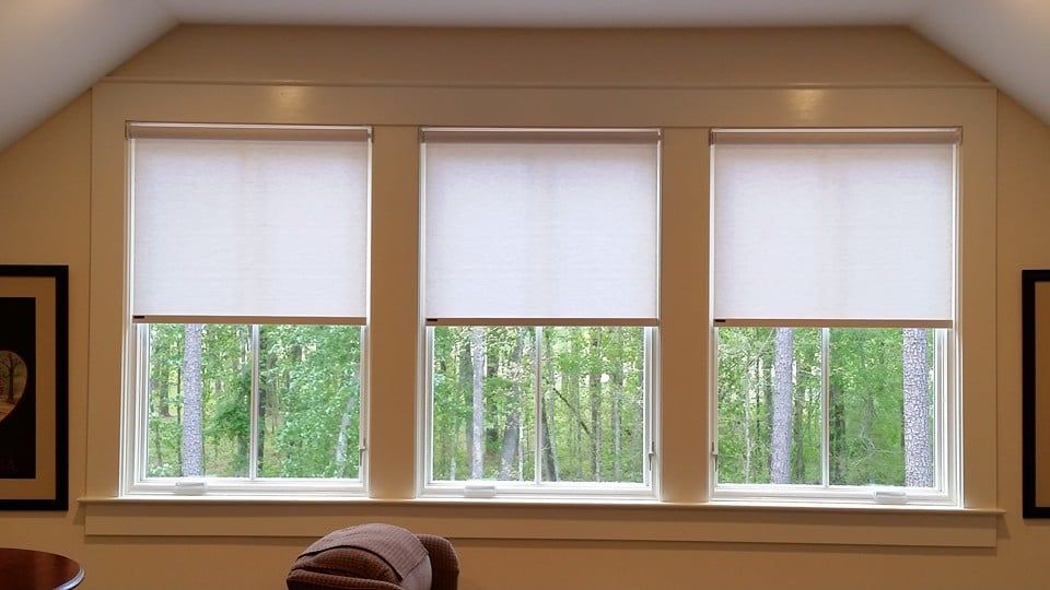 A living room with three windows and white blinds on them.