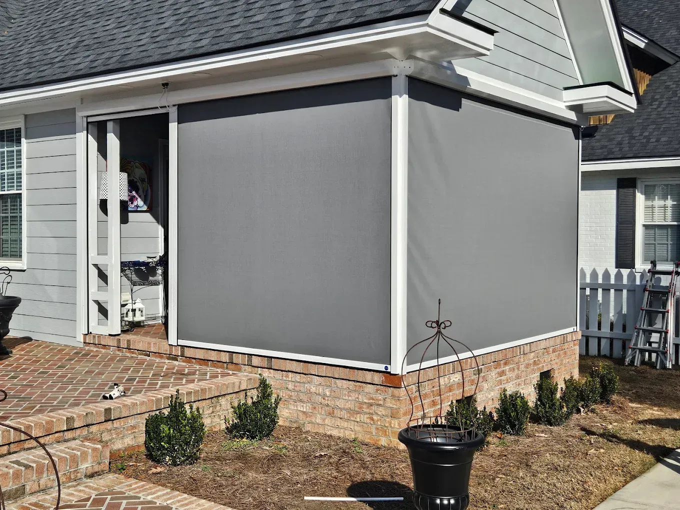 Gray house exterior with brick foundation, white trim, and small shrubs in the front yard