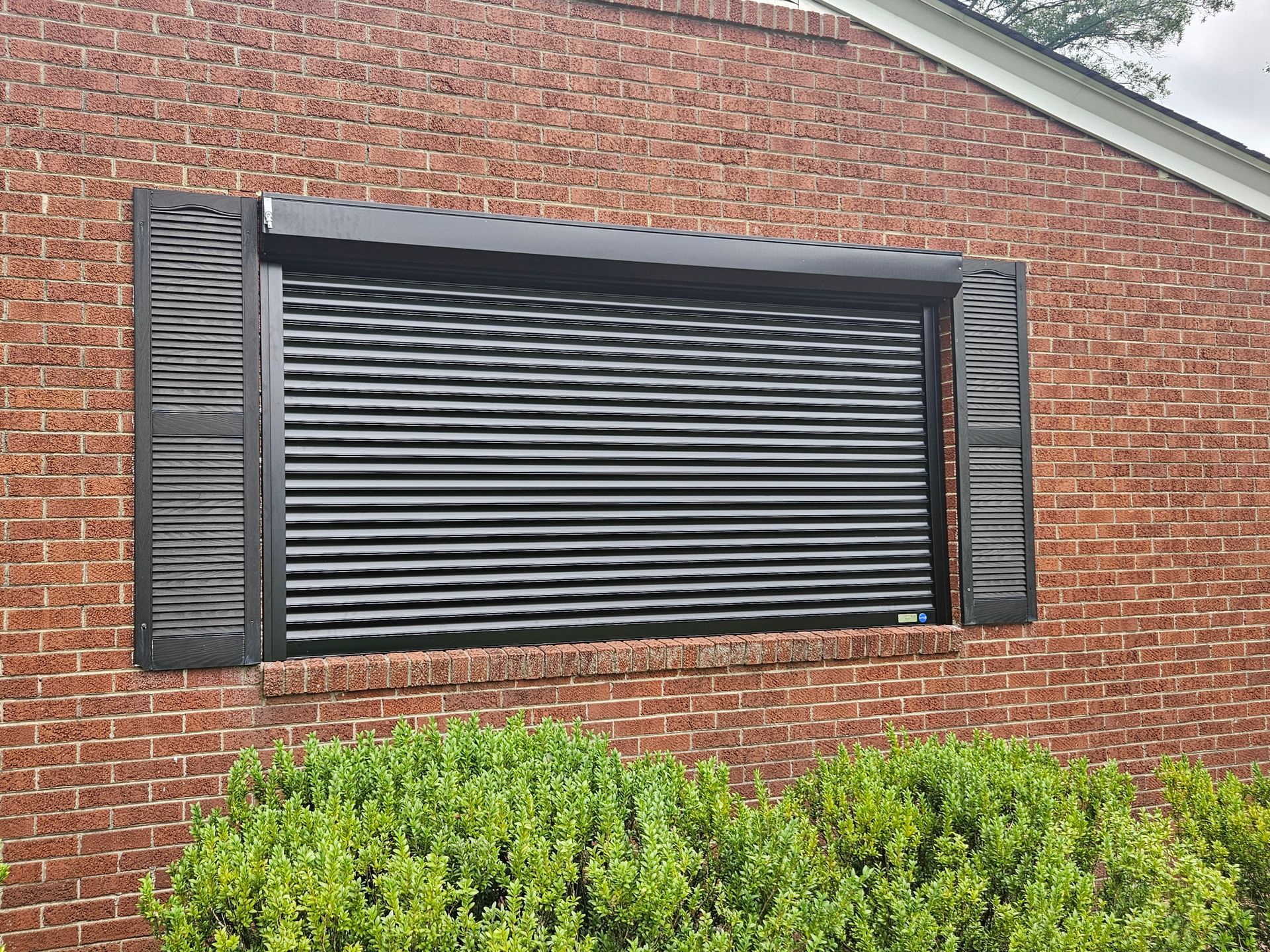 A brick building with a black shutter on the window.