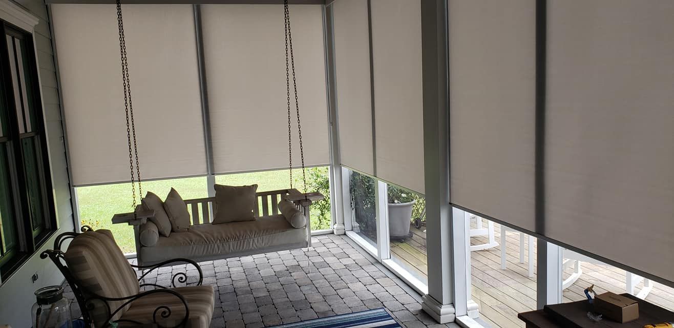 A porch with a swing , chairs , and blinds.