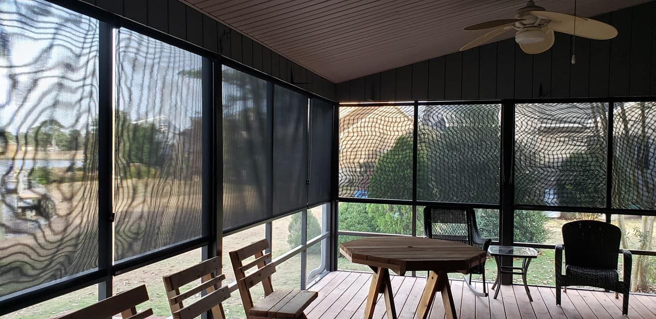 A screened in porch with a table and chairs and a ceiling fan.