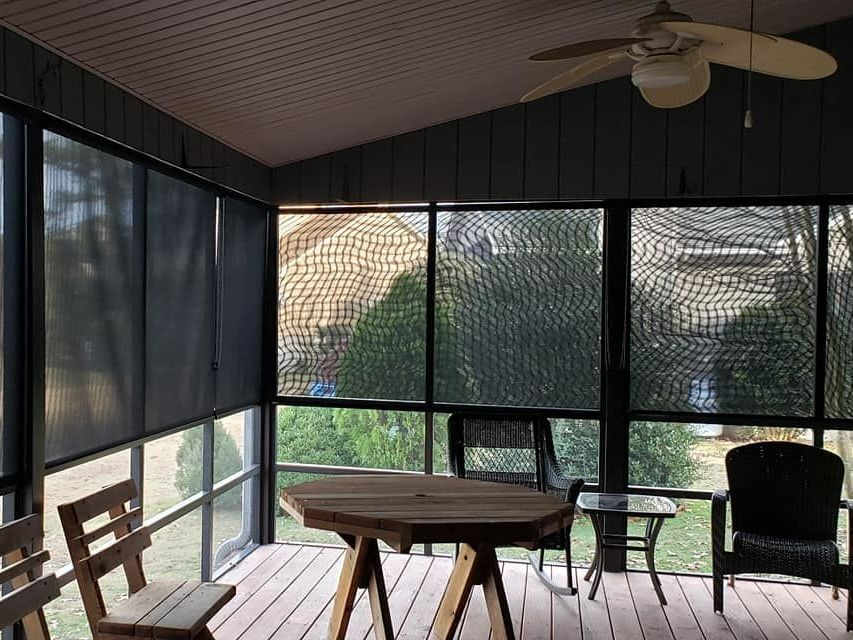 A screened in porch with a table and chairs and a ceiling fan