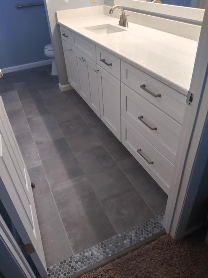 A bathroom with white cabinets , a sink , and a toilet.