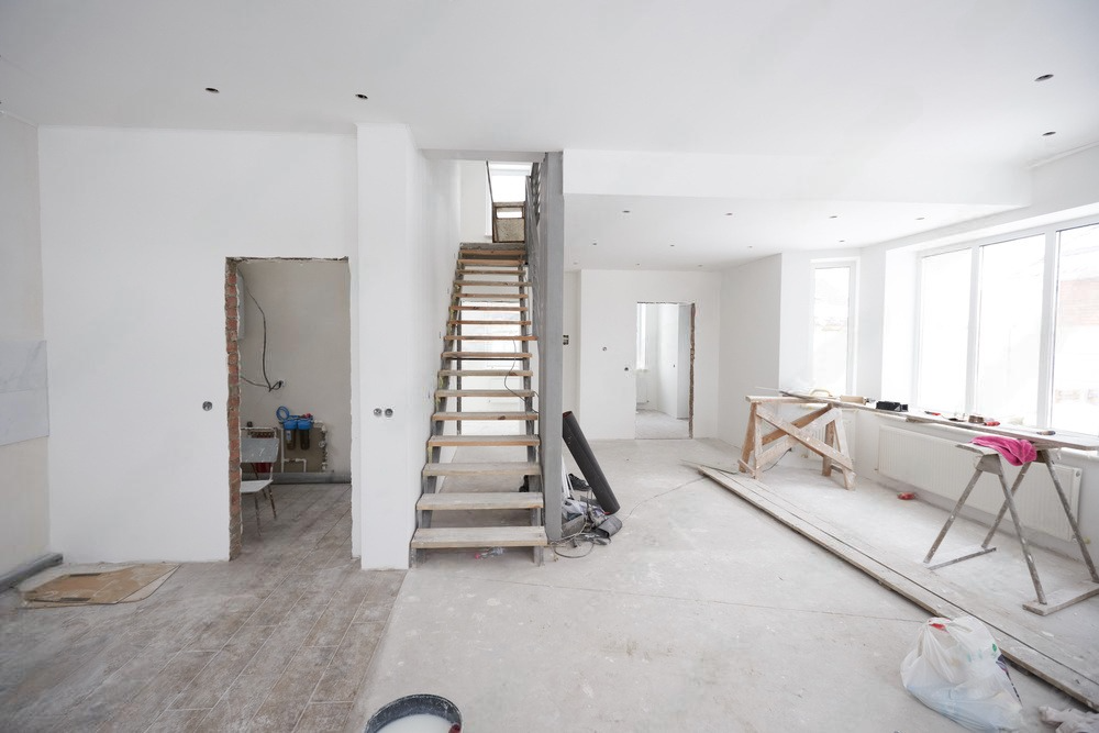 An unfinished house interior renovation project with exposed beams, bare walls, and scattered construction materials.