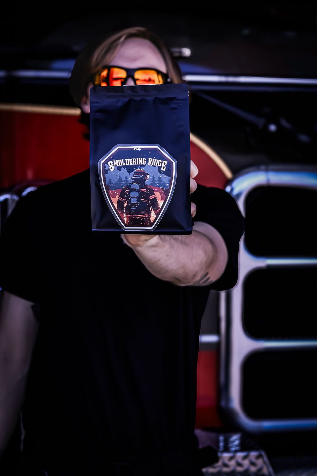 Man holding coffee bag with fiery logo in front of a truck.