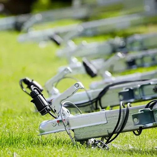 Row of silver trailer hitches on green grass, each with a black electrical connector.