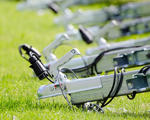 Silver trailer hitches on green grass, with electrical connectors visible.
