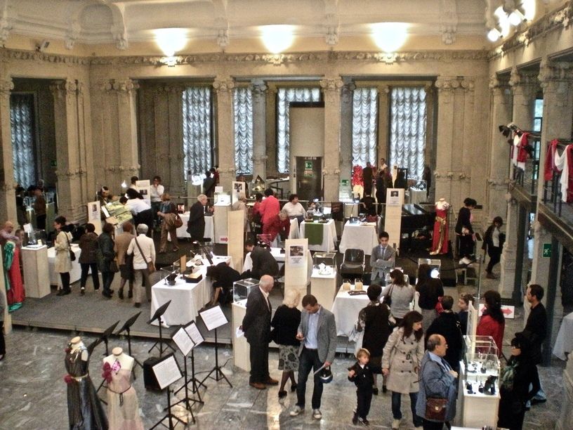 Le persone visitano le mostre durante un grande evento in un edificio classico con colonne e grandi finestre.