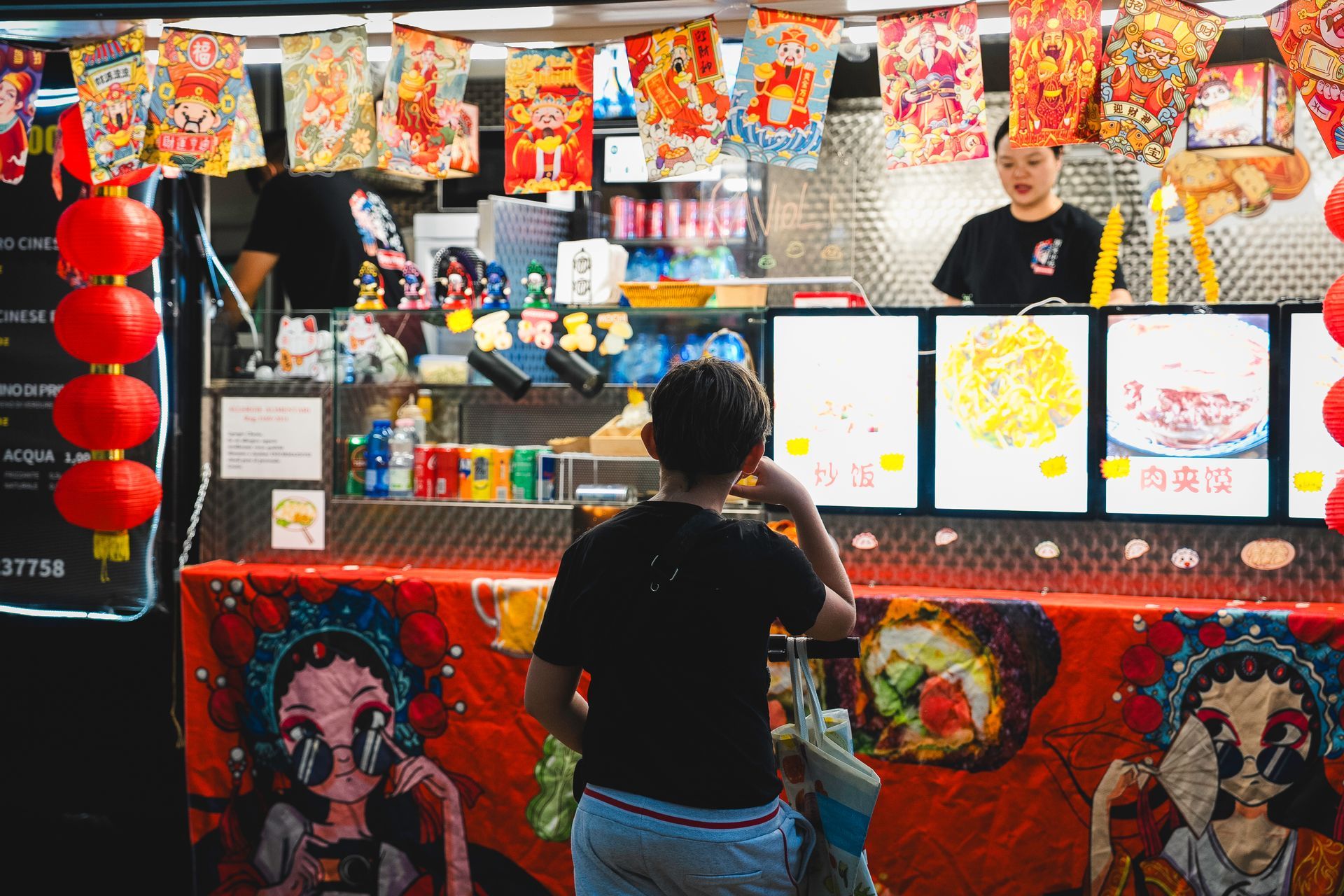 Ragazzo in una bancarella di cibo cinese con decorazioni colorate e un dipendente dietro il bancone.