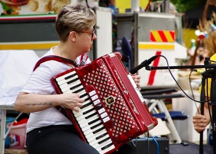 Donna con i capelli corti che suona una fisarmonica rossa all'aperto, vicino a un microfono.