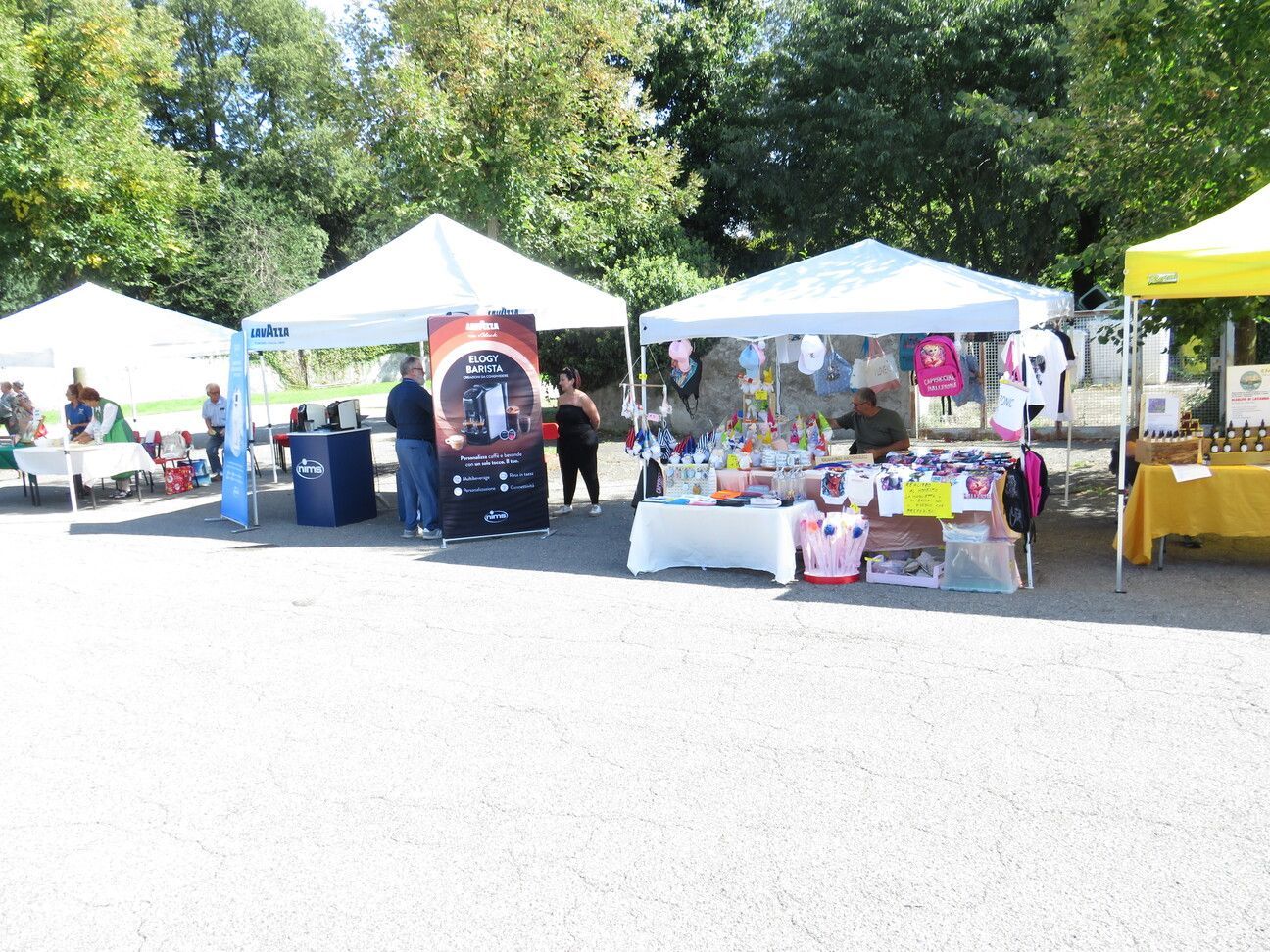 Mercato all'aperto con tende bianche e venditori che propongono merci sotto un cielo soleggiato.
