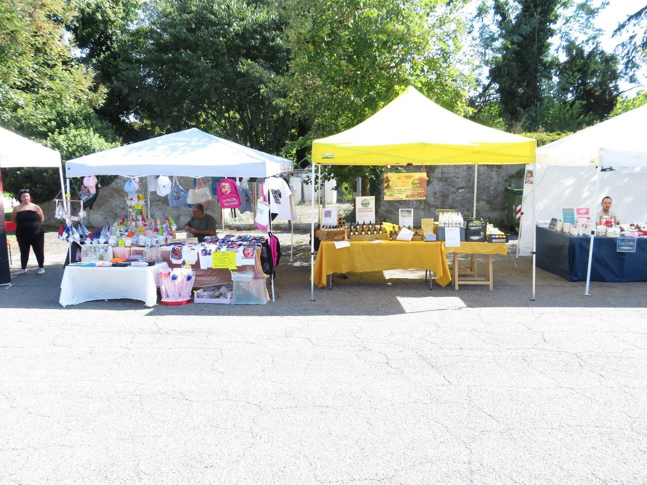 Mercato all'aperto con tende bianche e gialle che vendono merci su tavoli sotto un cielo soleggiato.