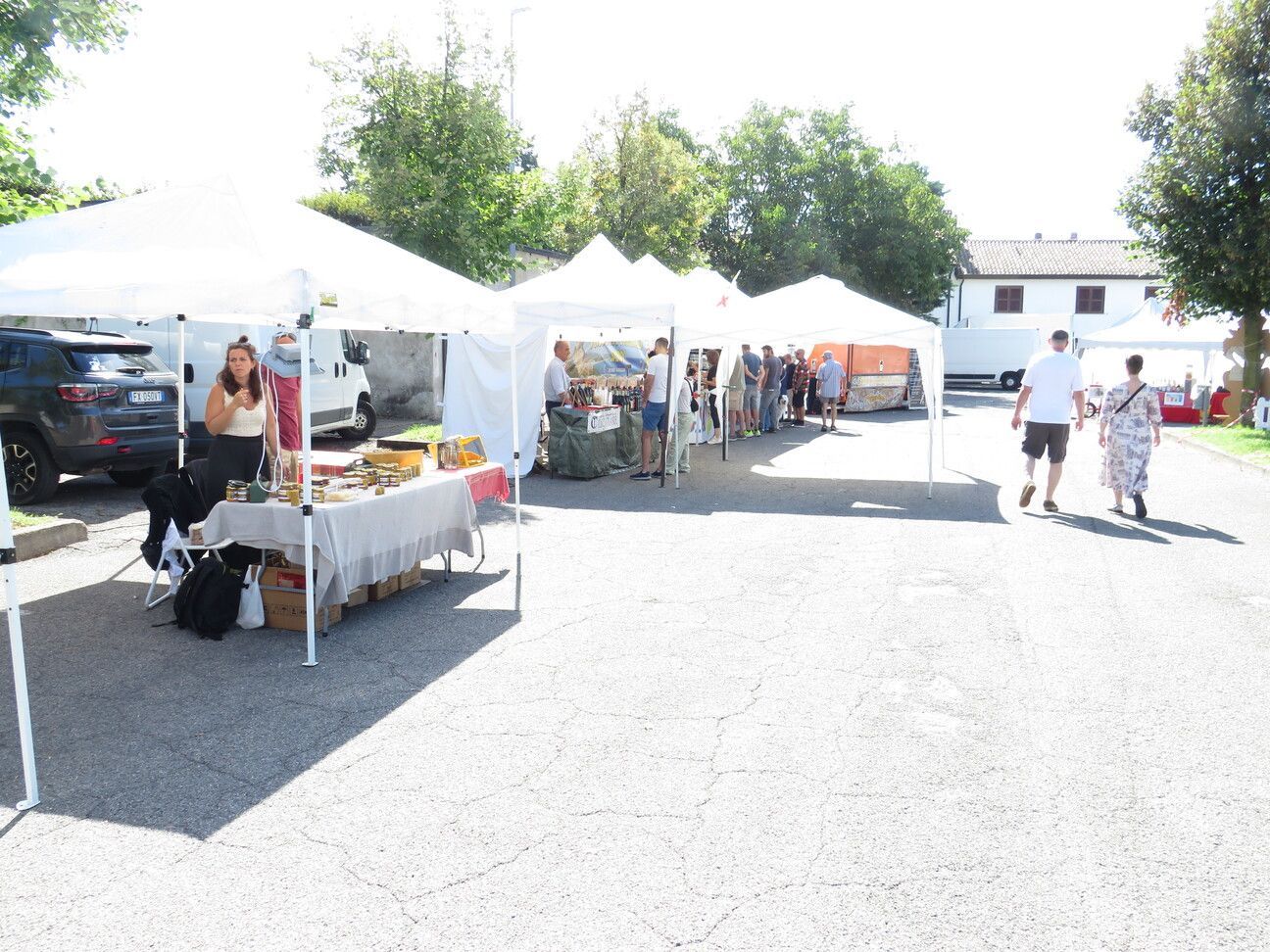 Mercato all'aperto con tende bianche, acquirenti e venditori in una giornata di sole.