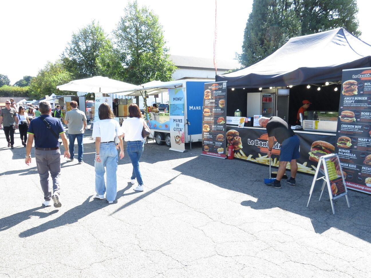 Bancarelle di cibo durante un evento all'aperto; gente che passeggia, giornata di sole.