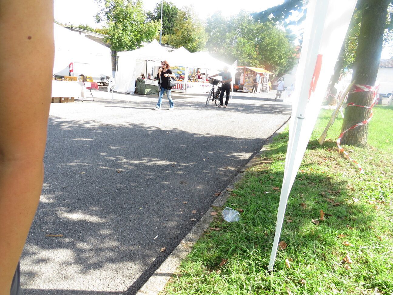 Scena di un mercato all'aperto soleggiato con venditori e persone su un sentiero lastricato. Una bandiera bianca è in primo piano.