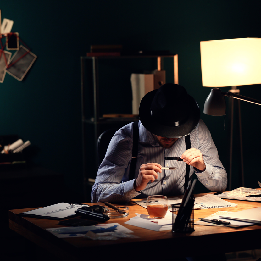 A man in a hat sits at a desk in a dark room