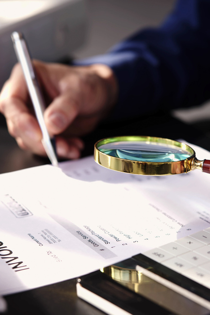 A person is writing on a piece of paper next to a magnifying glass.