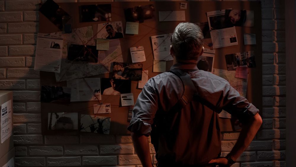 A man is standing in front of a bulletin board with a lot of papers on it.